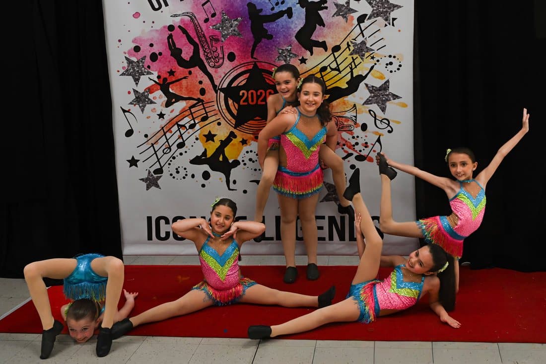 Dancers in rainbow costumes posing in splits and leaps