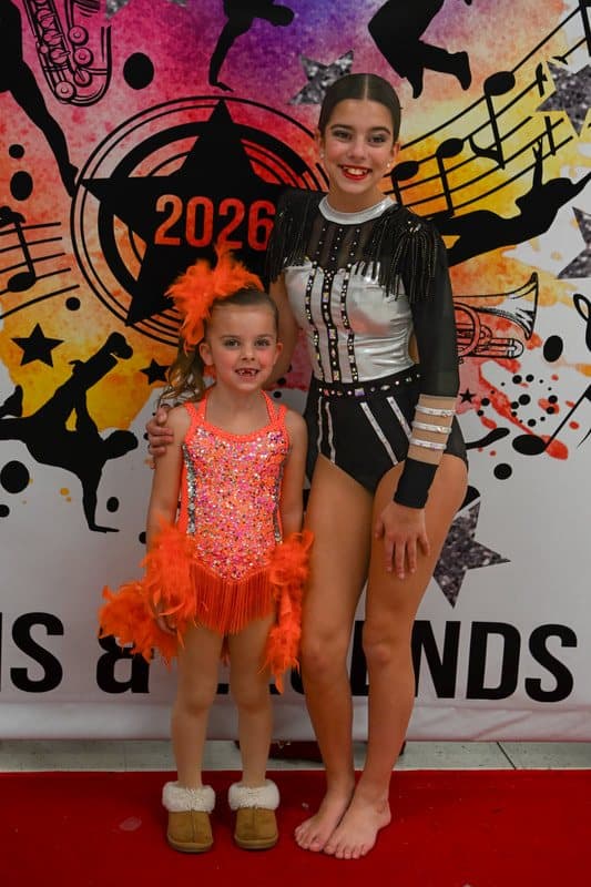 A tiny dancer in orange standing with an older dancer